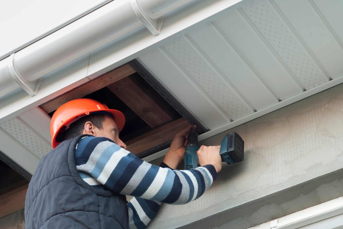 SoffitPro installer replacing a rotted fascia board with a cordless drill